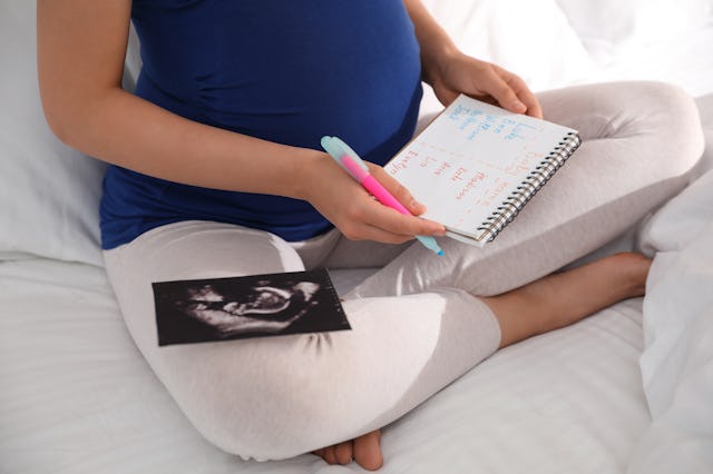 Pregnant woman with baby names list and sonogram sitting on bed, closeup