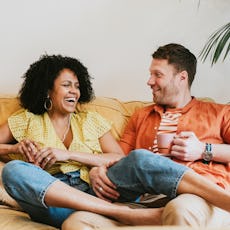 A couple sits on the couch, laughing together.