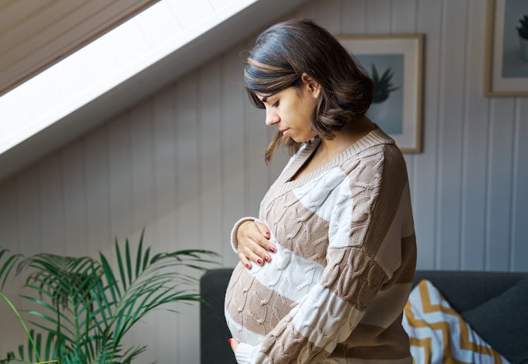 A pregnant woman looks down at her belly anxiously.