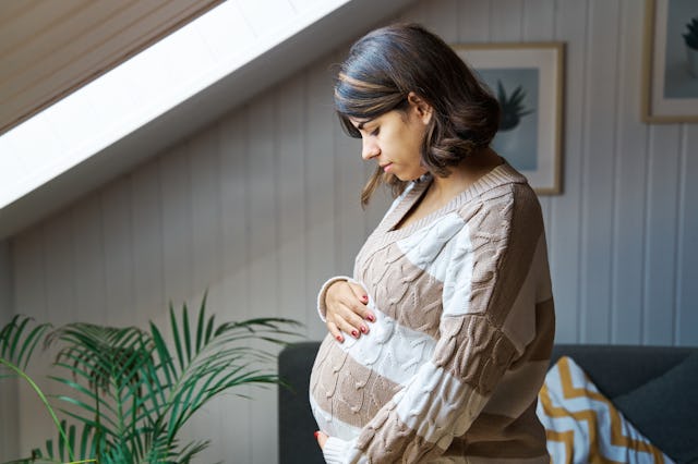 A pregnant woman looks down at her belly anxiously.