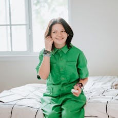 A nonbinary child sits on their bed with a cat.