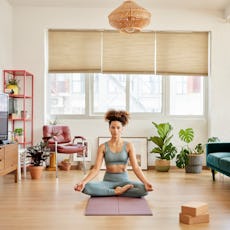 Full length of young woman meditating in living room. Woman practicing breathing exercise in living ...