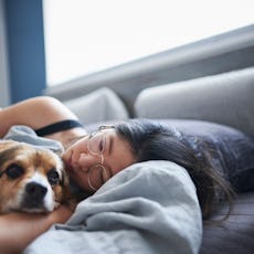 A woman lies in bed sick with her dog.