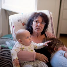 A grandma sits with her two grandkids in a rocking chair.