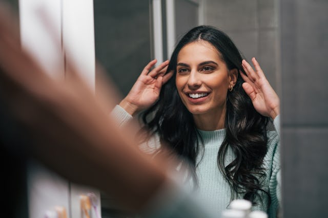 A woman looks at her hair curls in the mirror.