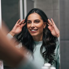 A woman looks at her hair curls in the mirror.