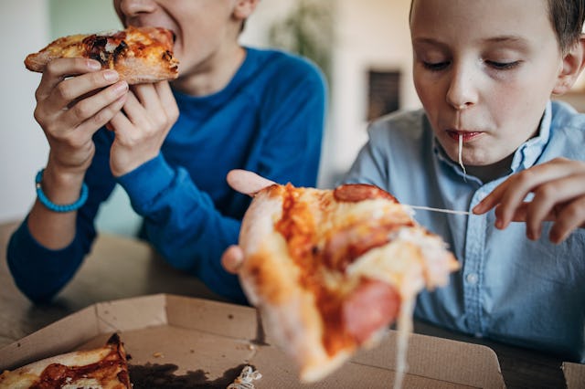 Two boys, two brothers sitting in dining room at home, eating pizza together.