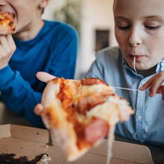 Two boys, two brothers sitting in dining room at home, eating pizza together.