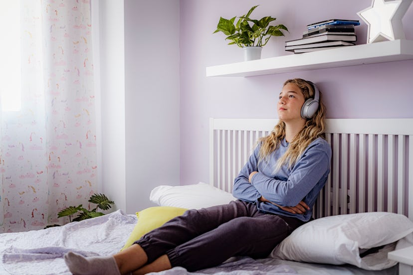 A teen sits in a pale purple room.