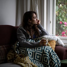 A woman sits alone in her living room, looking out of the window and reflecting.