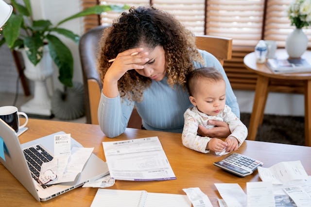 A stressed-out woman looks at her bills and holds her baby.