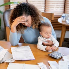 A stressed-out woman looks at her bills and holds her baby.