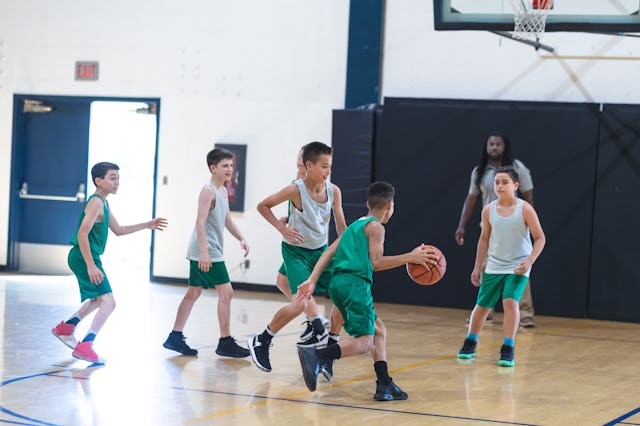 A young African American boy dribbles around his defender and tries to score. Coach is standing on t...