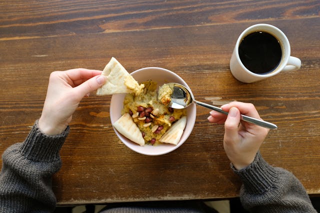 A large bowl of hummus, garnished and sprinkled with pomegranate, spices and roasted peanuts and nut...