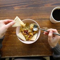 A large bowl of hummus, garnished and sprinkled with pomegranate, spices and roasted peanuts and nut...