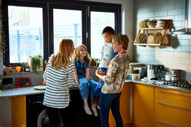 Little girl sitting on a kitchen counter and talking with her mum and adoptive parents