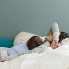 A woman who isn't feeling well lays in bed with her child.