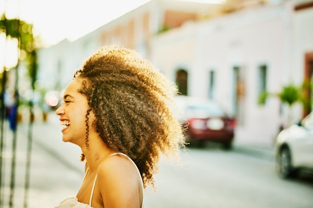 A girl with curly hair wearing a white dress smiling while the sun reflects on her hair