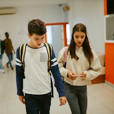 A young teen couple walks together in the hall at school.