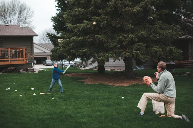 Boy hits a baseball into the air with a bat that his father has just pitched to him while practicing...