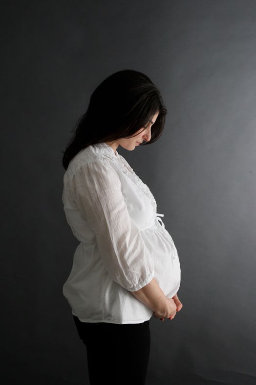 A young pregnant woman with long black hair looking at her stomach