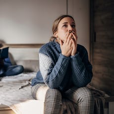 A woman sits on the end of the bed after an argument with her husband.