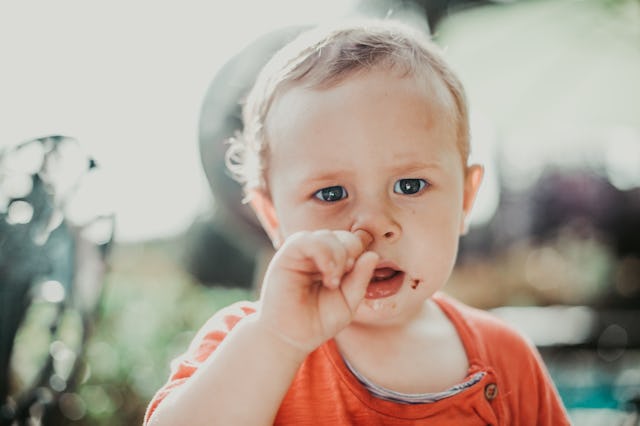 Blue-eyed baby picking his nose while wearing an orange shirt