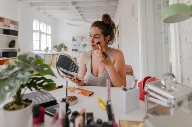 A woman applies makeup to her face.