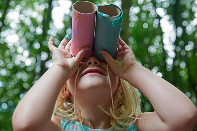 Four year old girl looking up through home made toy binocolors in forest