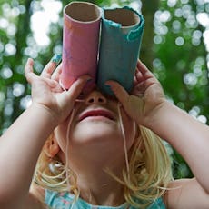 Four year old girl looking up through home made toy binocolors in forest