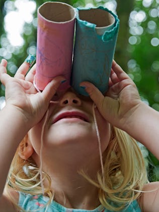 Four year old girl looking up through home made toy binocolors in forest