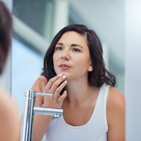 A woman looks at her face in the mirror.