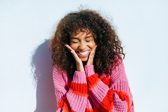 A woman smiles, holding her face.