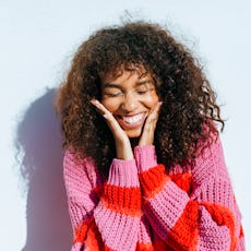 A woman smiles, holding her face.