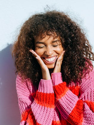 A woman smiles, holding her face.