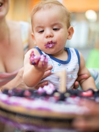 Toddler with cake on face at birthday party, surrounded by laughing family members.