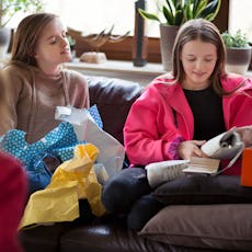 A group of teens open birthday presents on the couch.