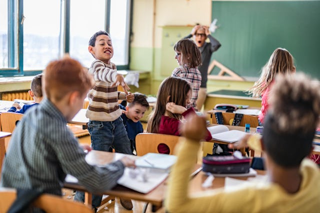 Children cause chaos in a classroom as a teacher looks on.