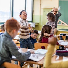 Children cause chaos in a classroom as a teacher looks on.