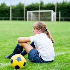 A young soccer player sits on a field, defeated.