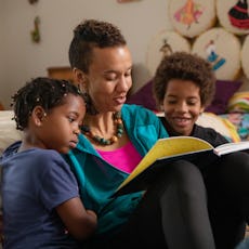 A woman reading a book to two children in a cozy, colorful room decorated with artistic elements.