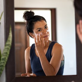 A woman applies sunscreen to her face.