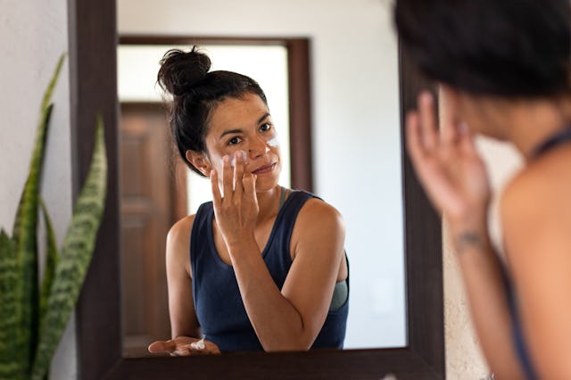 A woman applies sunscreen to her face.