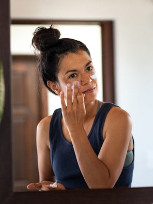 A woman applies sunscreen to her face.