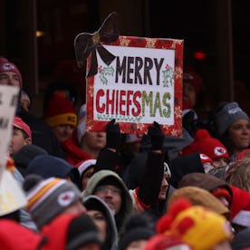 Crowd of Kansas City Chiefs fans with a sign reading "Merry Chiefsmas" at a football game.