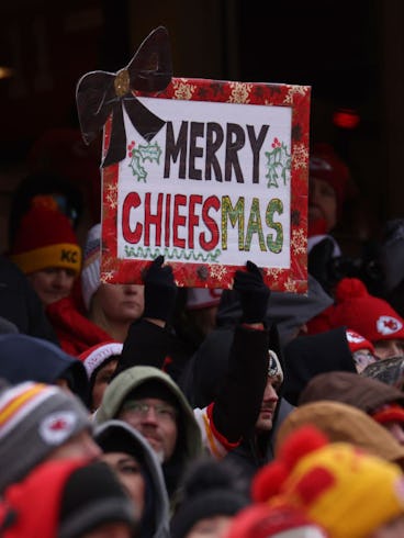 Crowd of Kansas City Chiefs fans with a sign reading "Merry Chiefsmas" at a football game.