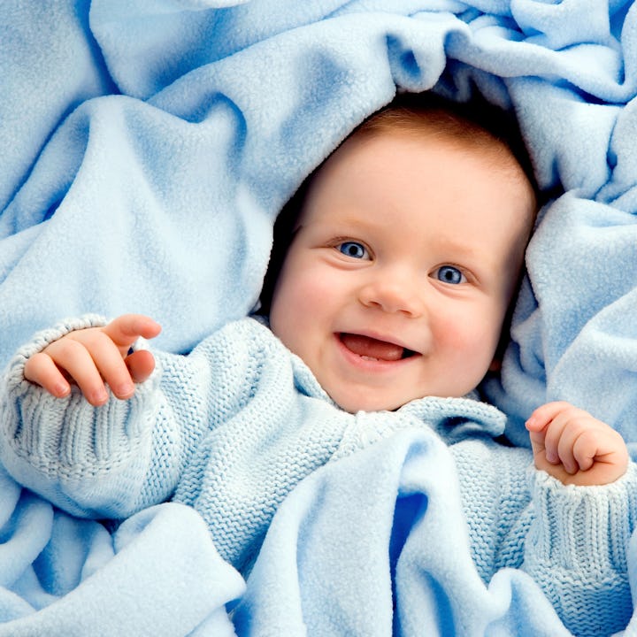 A joyful baby in a blue sweater wrapped in a soft blue blanket, smiling happily.