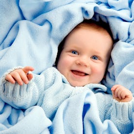 A joyful baby in a blue sweater wrapped in a soft blue blanket, smiling happily.