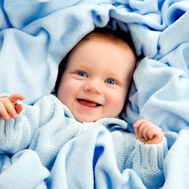 A joyful baby in a blue sweater wrapped in a soft blue blanket, smiling happily.