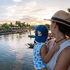 Young woman holding her child in her arms while admiring the Thu Bon river at sunset.